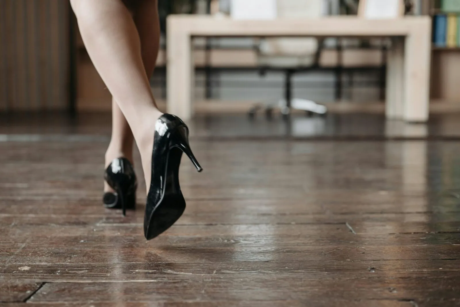 Pés de mulher com sapatos de salto alto sobre piso de madeira